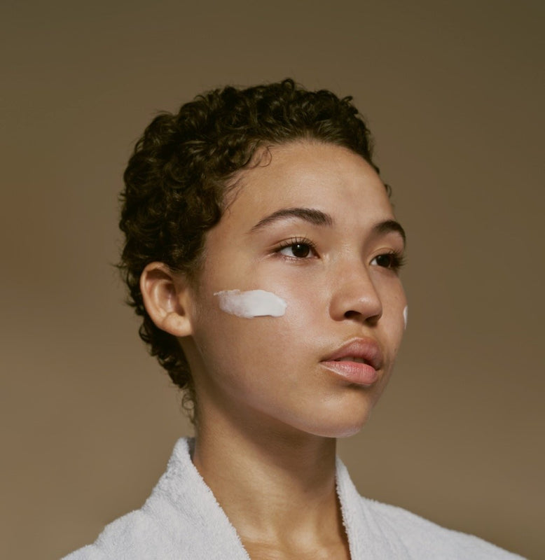 Woman of color with thick creamy moisturizer on cheek